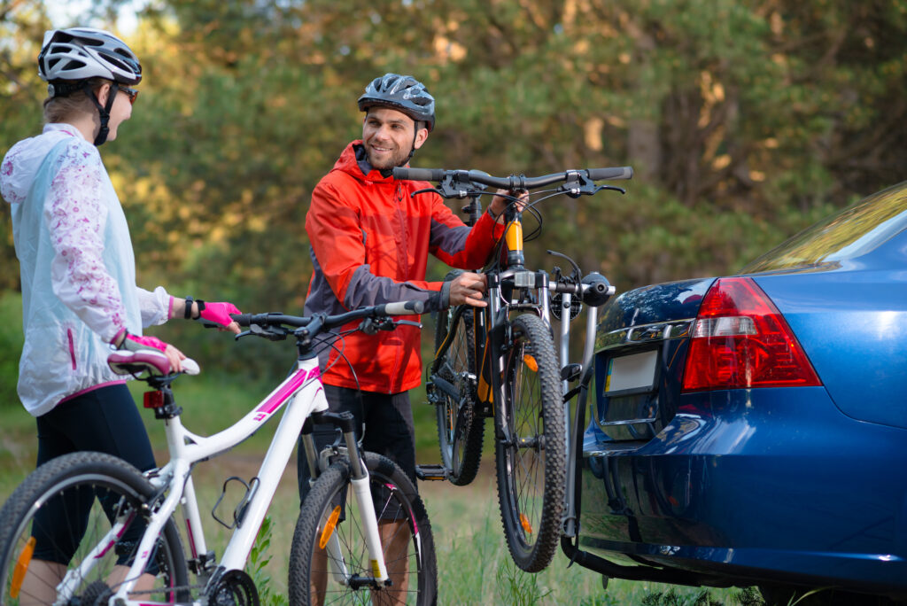 Young Couple Unmounting Mountain Bikes From Bike Rack On The Car. Adventure And Family Travel Concept.